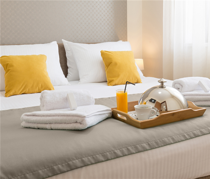 Hotel bed with room service on bed and grey, white and yellow bedding